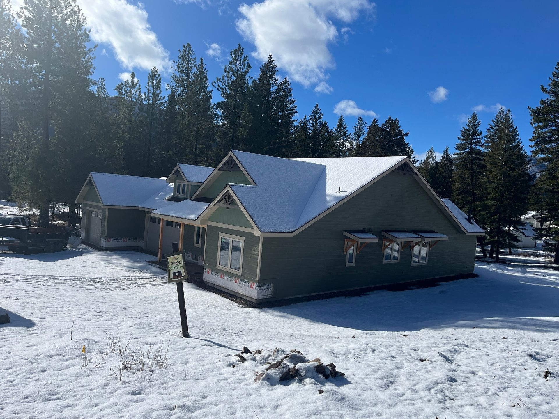 Snow-covered cabin with gray siding and white roof in a sunny forest clearing