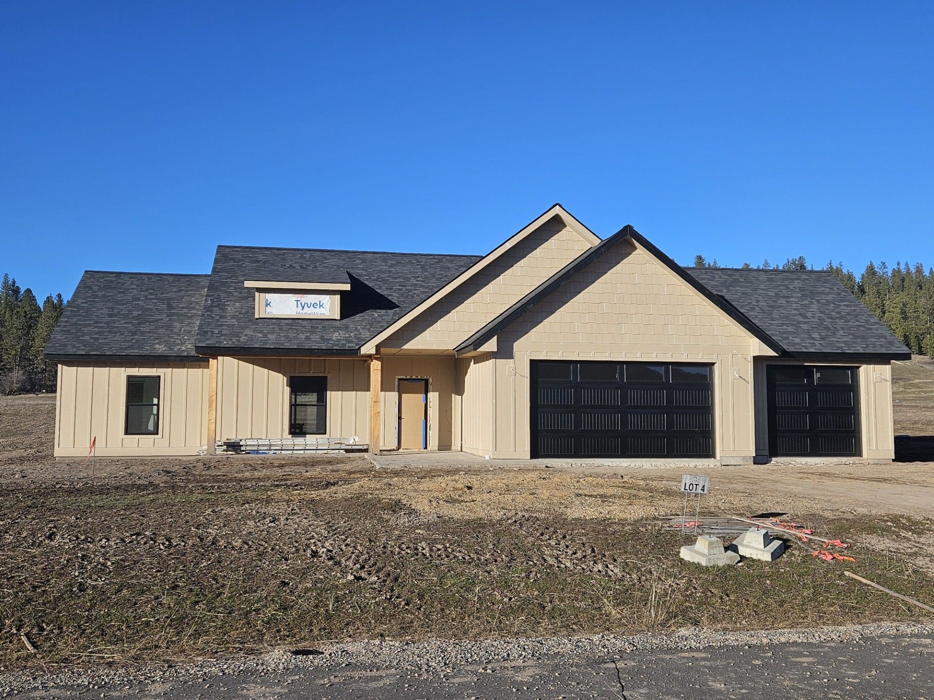 Single-story beige house with a dark roof and large black garage doors under a clear blue sky