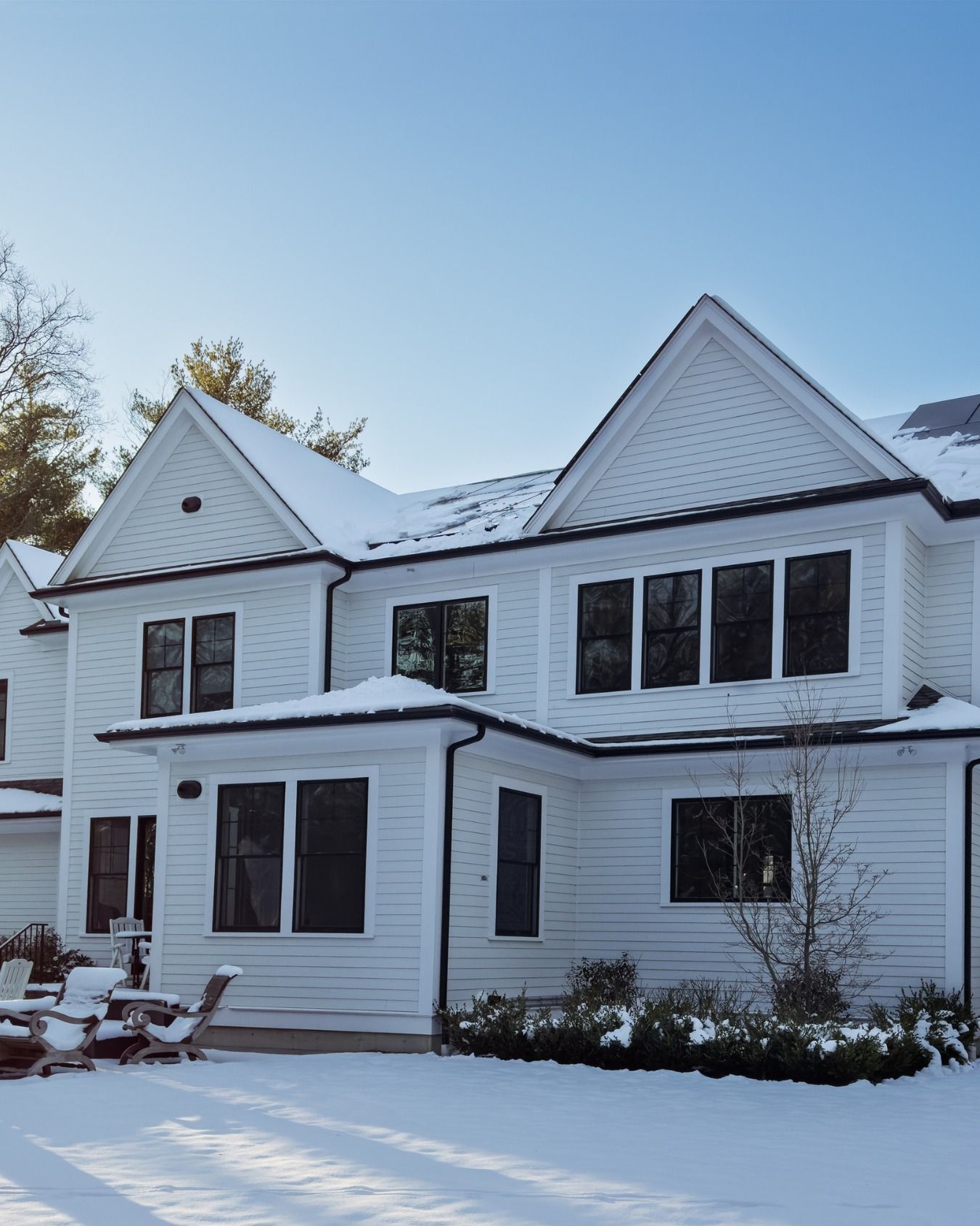 Snow-covered white house with black shutters under a clear blue sky