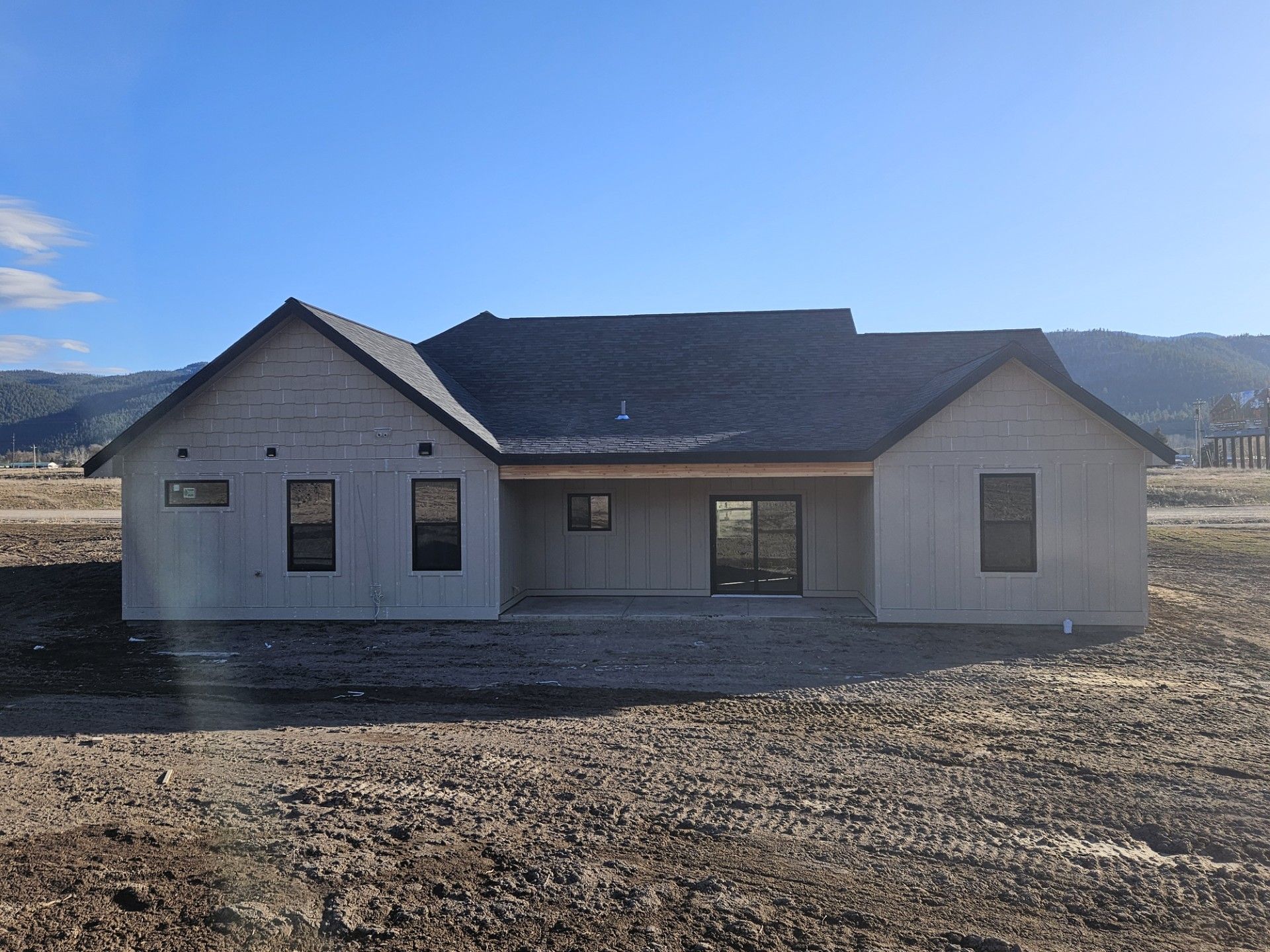 Single-story gray house under construction on a bare lot with mountains in the background