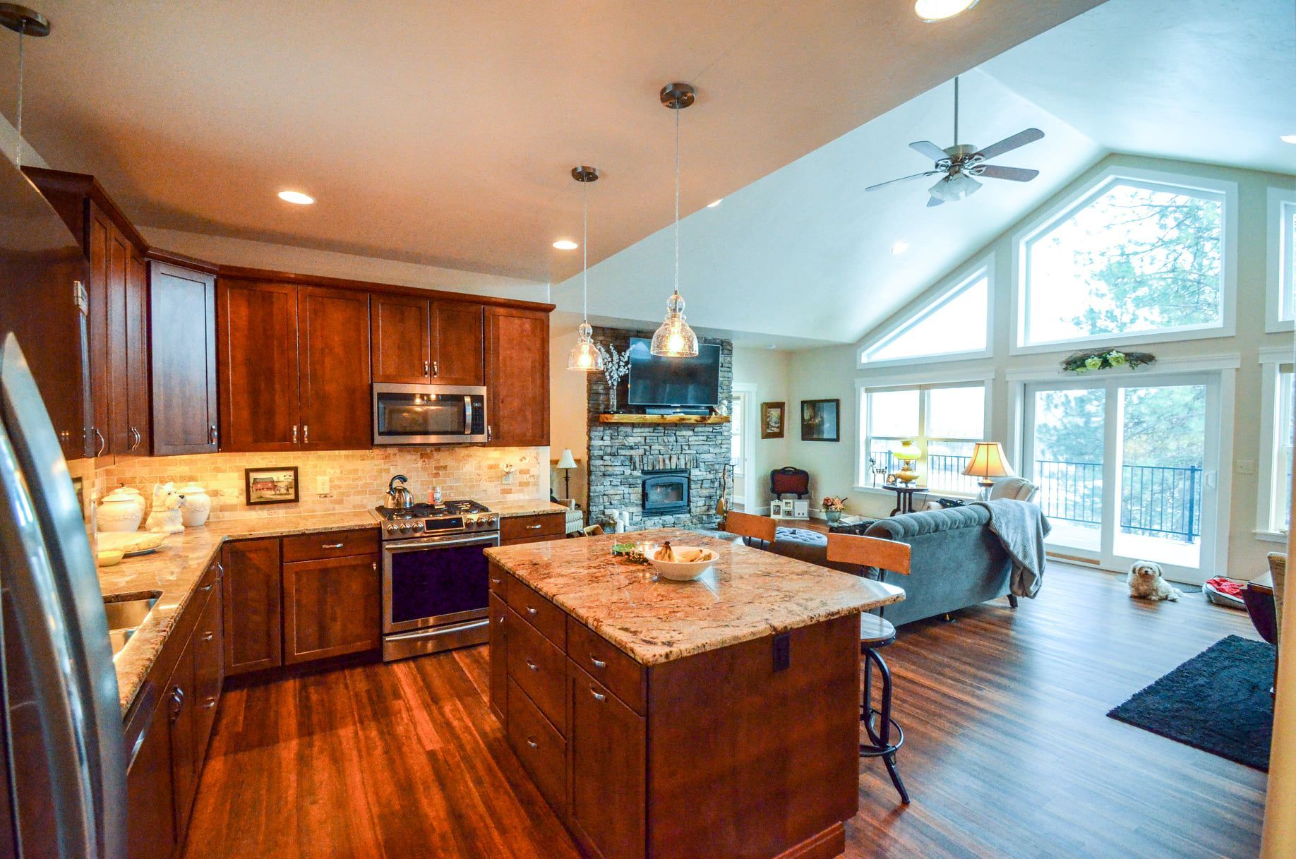 Modern open-plan kitchen and living room with wood floors, island, high windows, and a vaulted ceiling
