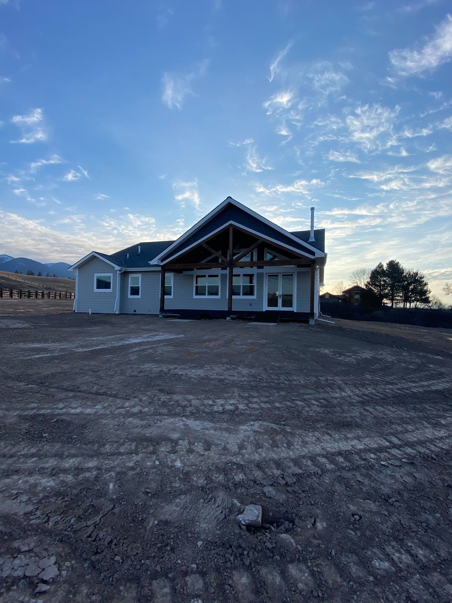 Small white house under construction on a dirt lot beneath a blue, partly cloudy sky.