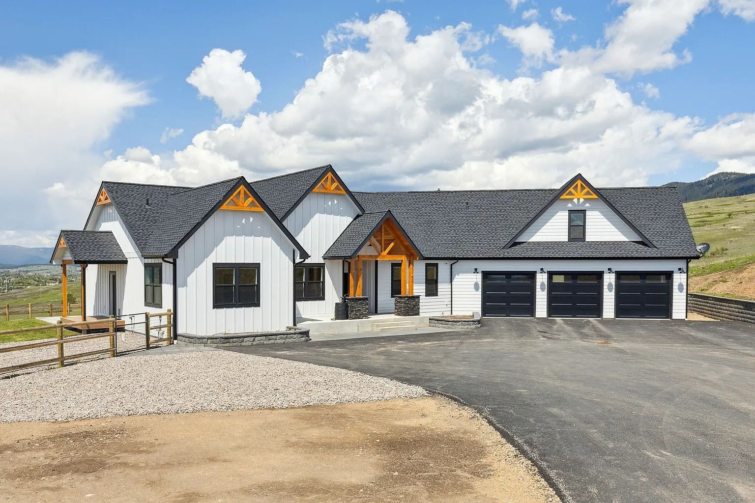 New modern white house with gray roof, black garage doors, and gravel driveway under a partly cloudy sky