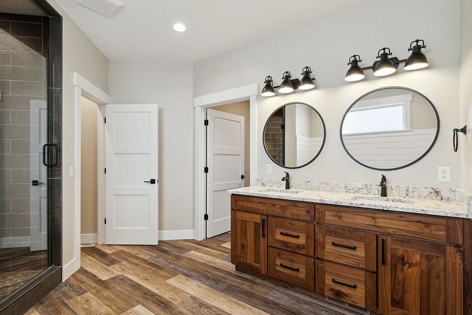 Spacious bathroom with double wooden vanity, round mirrors, granite countertop, and tiled shower