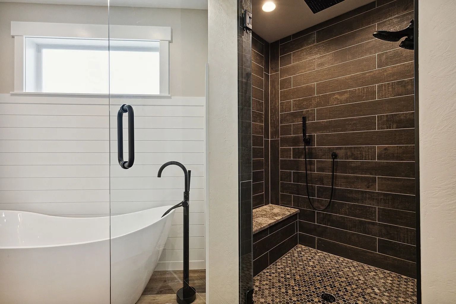 Modern bathroom with freestanding tub and glass-enclosed dark tiled shower with pebble floor