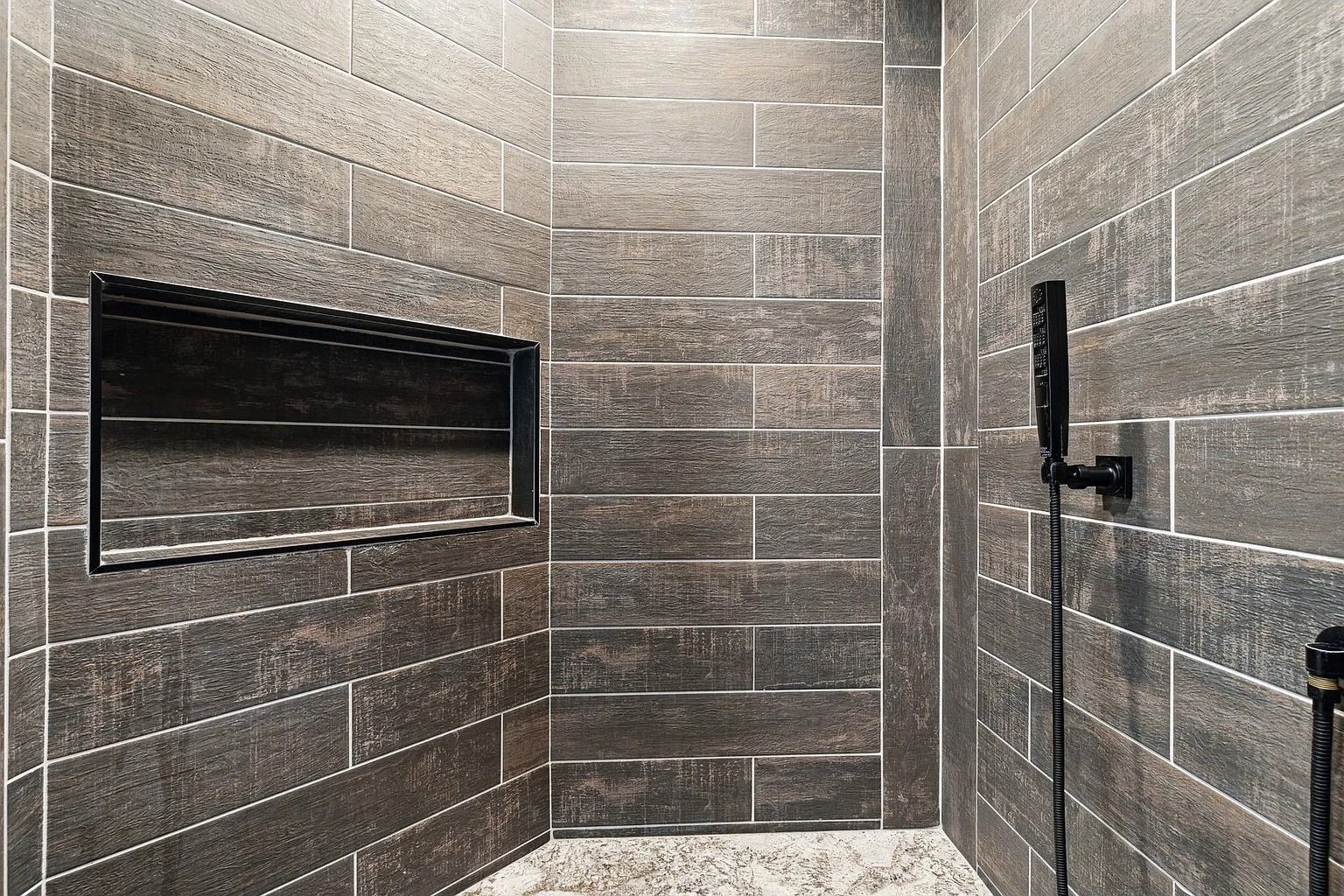 Modern tiled shower with a wall niche and black grab bars in a gray bathroom