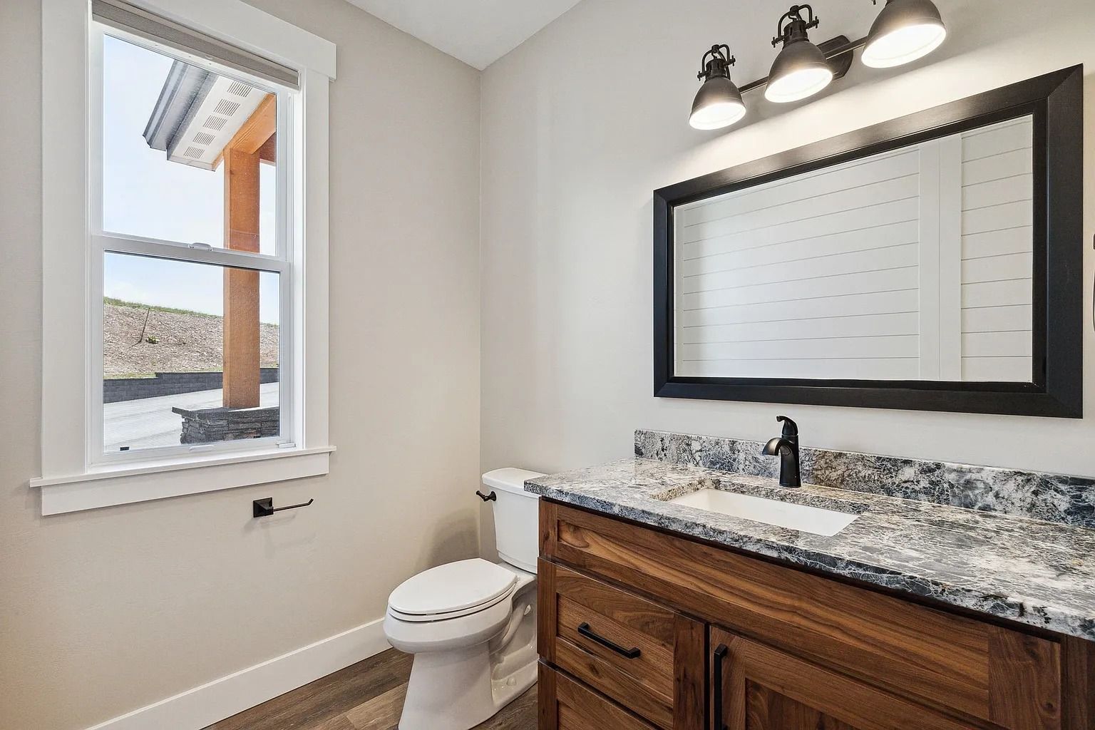 Bathroom vanity with granite countertop, mirror, toilet, and window with snowy view
