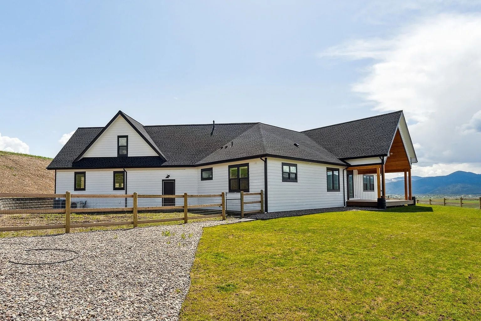 Modern white house with dark roof beside a gravel drive and green lawn under a blue sky