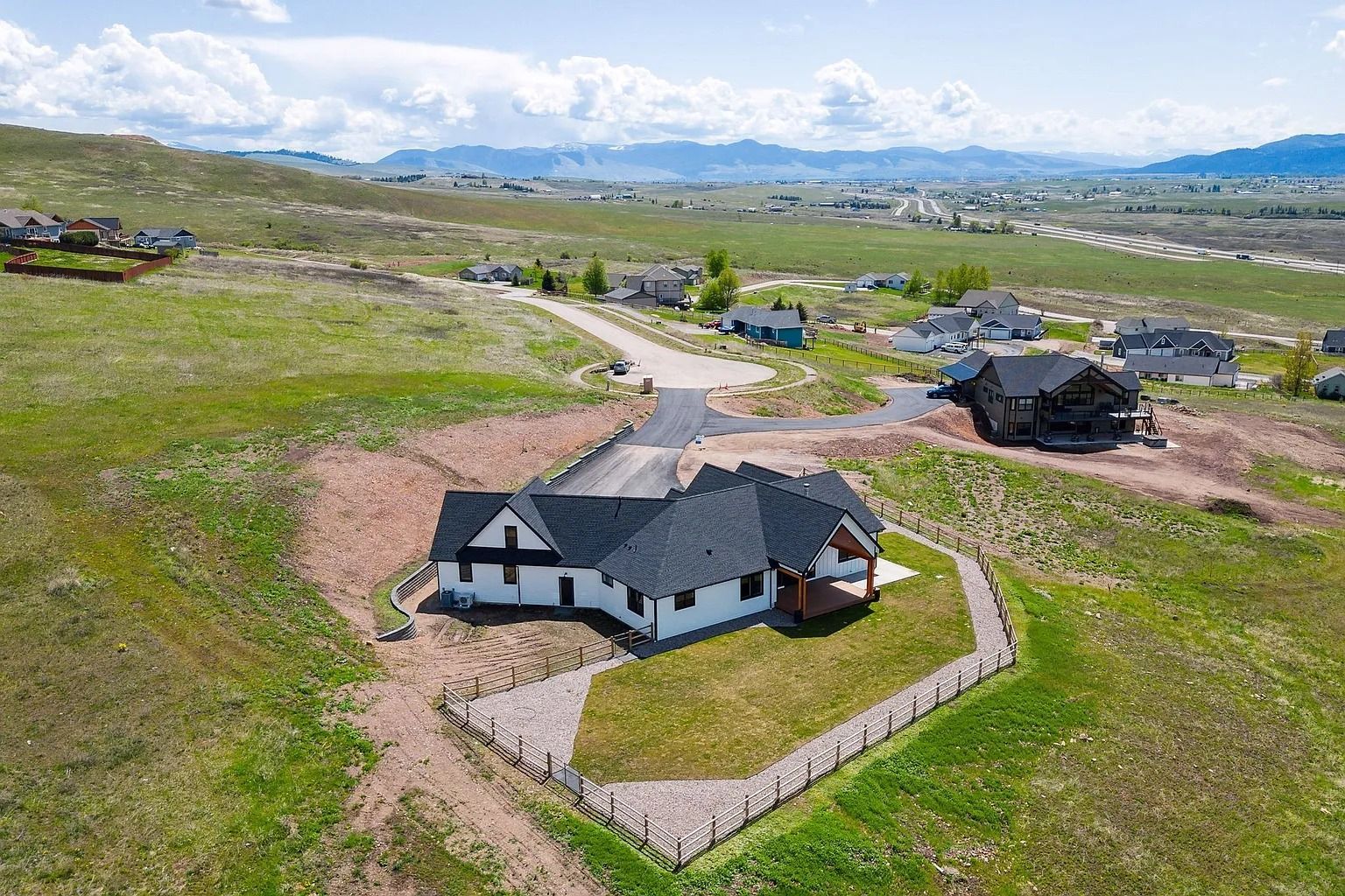 Aerial view of a white house with a dark roof on a grassy hillside near a winding road.