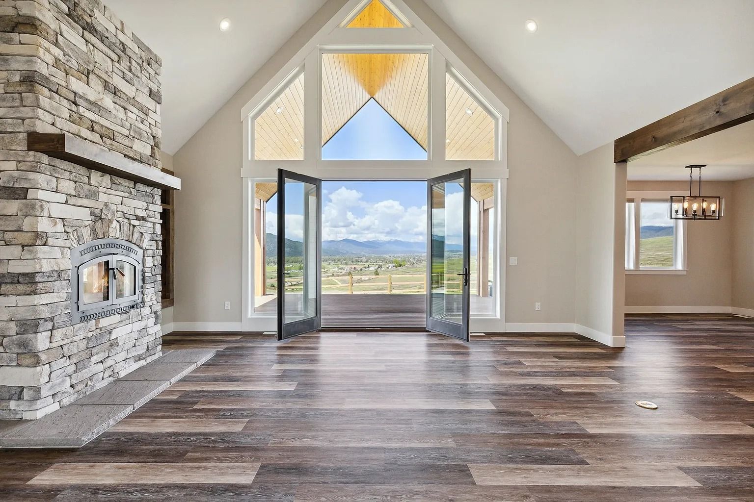 Spacious living room with stone fireplace, dark wood floors, and open French doors to a mountain view.
