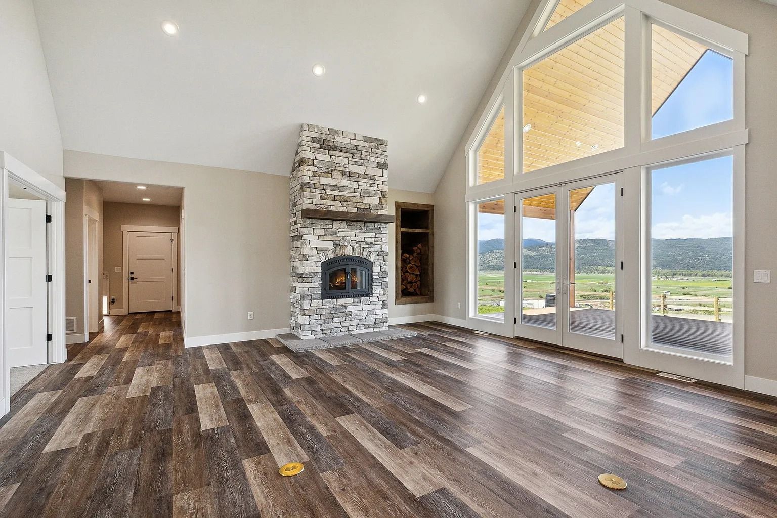 Spacious living room with stone fireplace, vaulted ceiling, wood floors, and large windows overlooking greenery