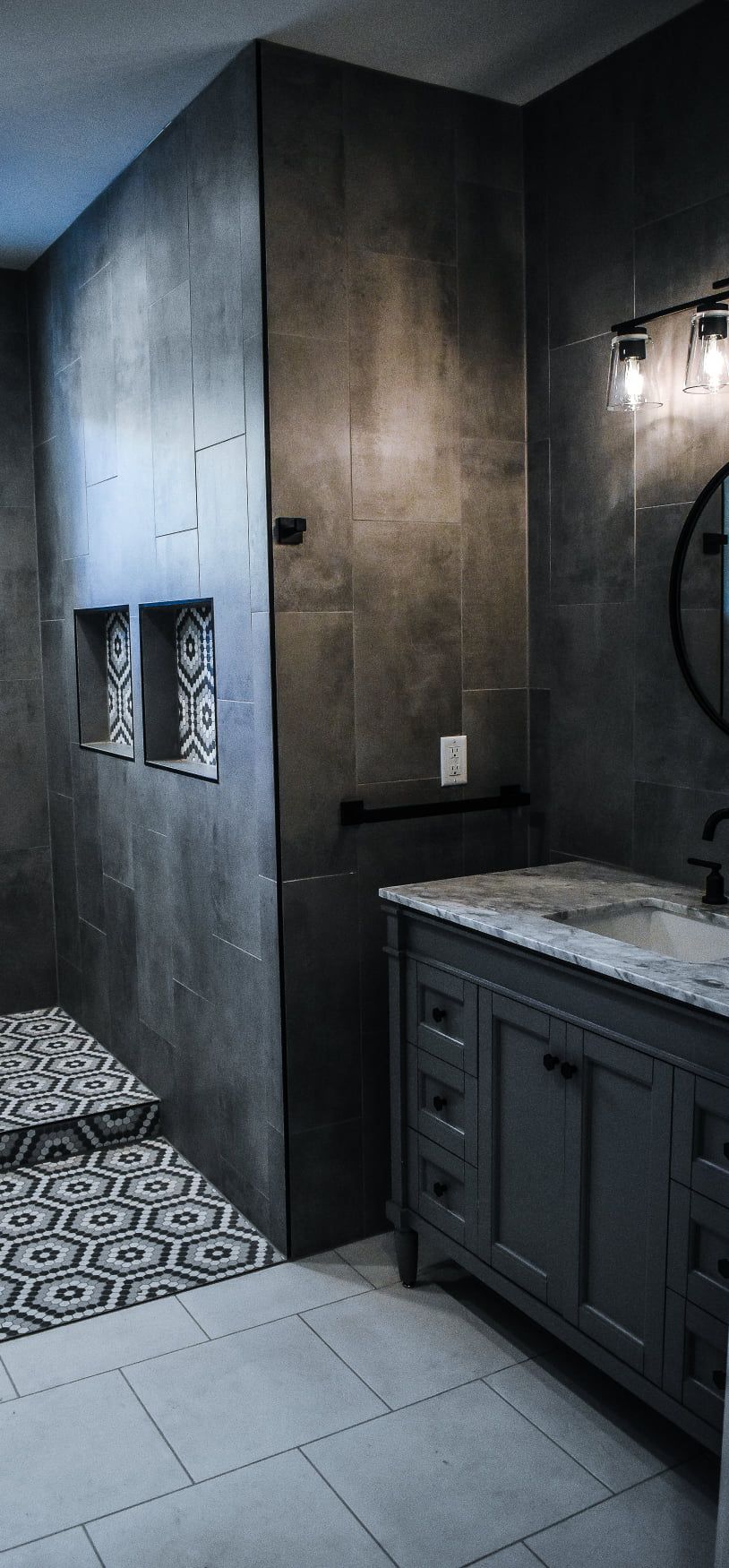 Modern dark bathroom with patterned tile floor, marble vanity, and built-in wall niches.