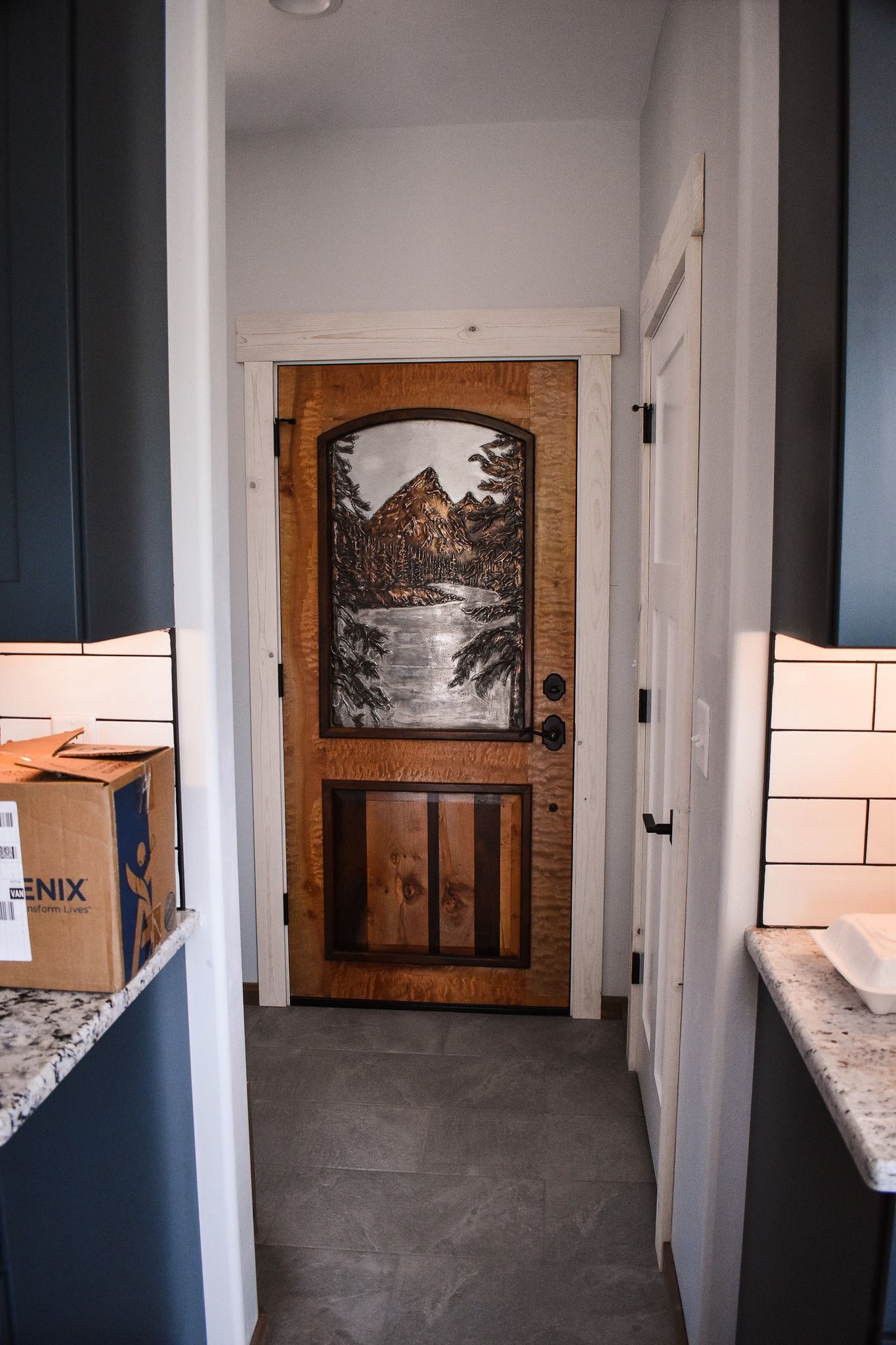 Narrow kitchen hallway with a carved wooden door at the end and boxes on both sides.