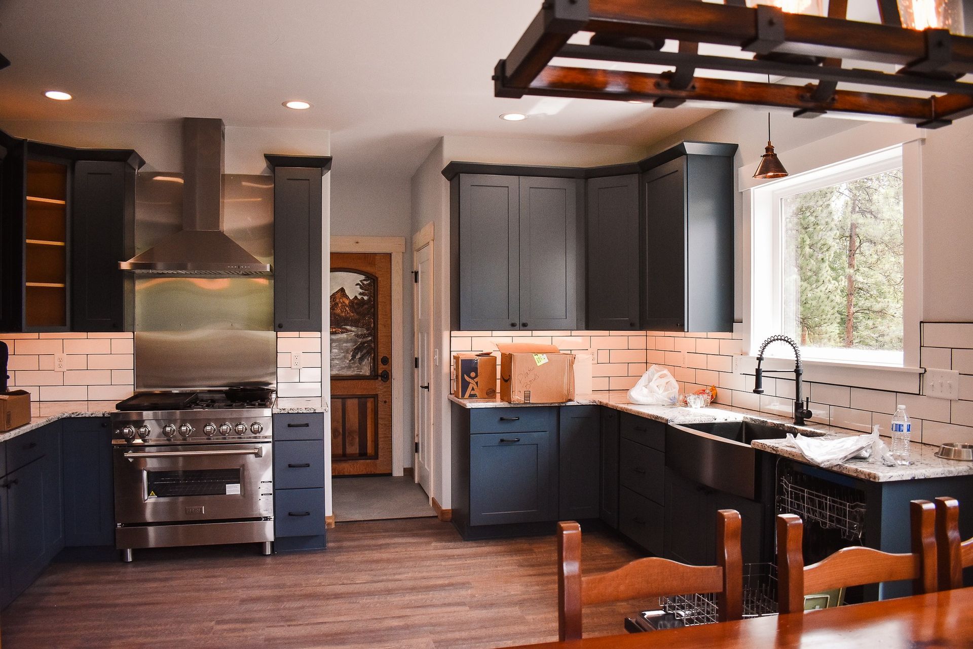 Modern kitchen with dark cabinets, stainless stove, granite island, and large window over the sink