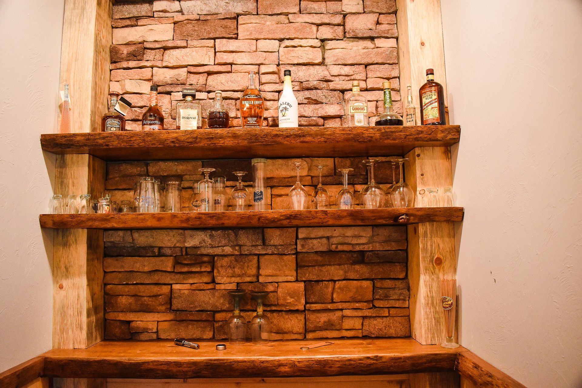 Wooden mantel with stone backdrop and shelves holding assorted glass bottles and decor