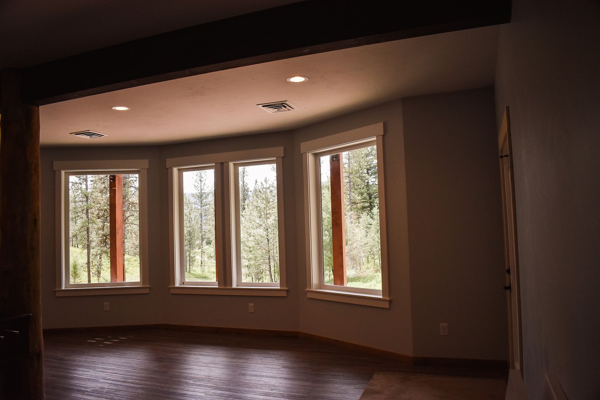 Empty room with curved bay windows, wood floor, and warm light from trees outside