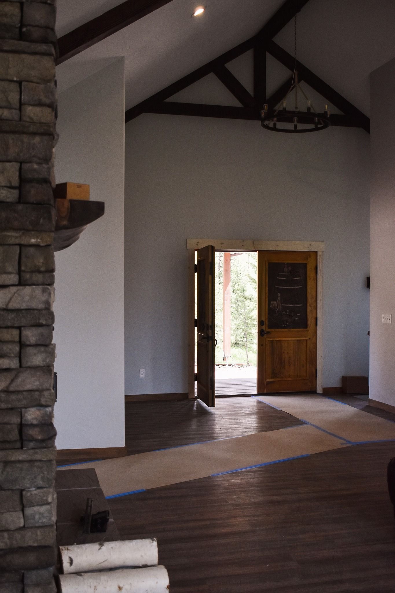 Empty modern interior with vaulted ceiling, dark wood floors, stone fireplace, and open wooden door to outside