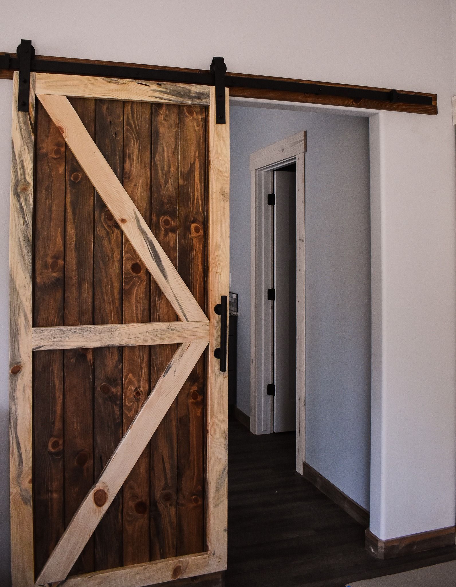 Open wooden barn door in a white hallway with a dark floor and an open doorway beyond
