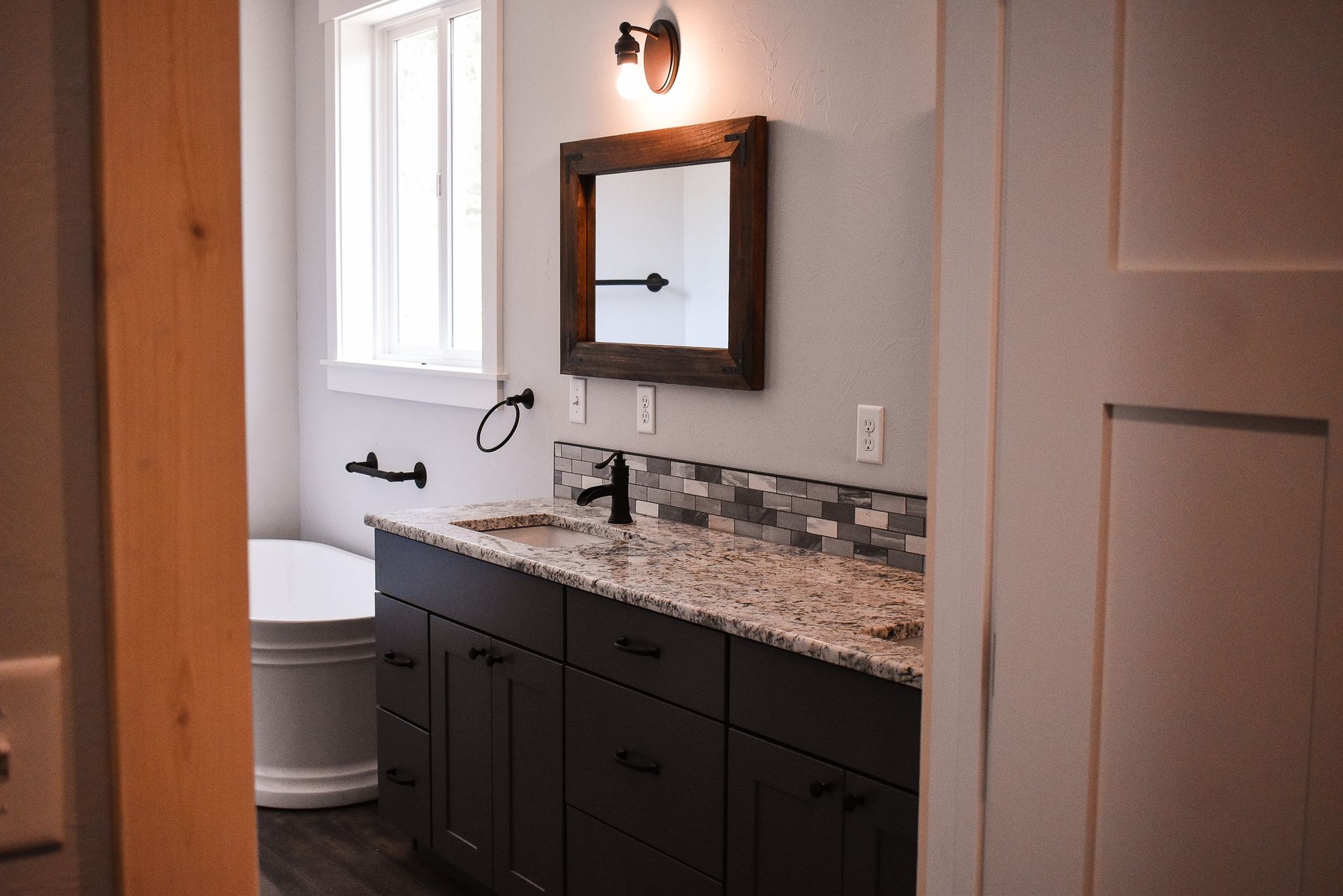 Small bathroom with dark vanity, granite countertop, mirror, and toilet beside a wooden door.