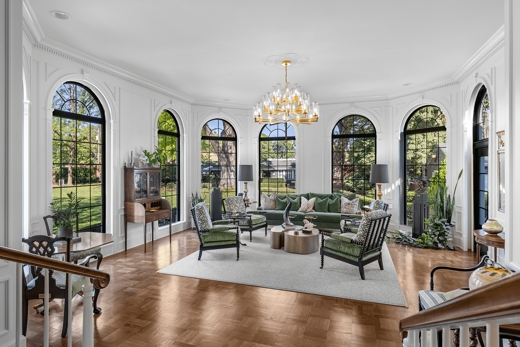 Elegant white living room with arched windows, chandelier, and green-and-black seating around a coffee table.