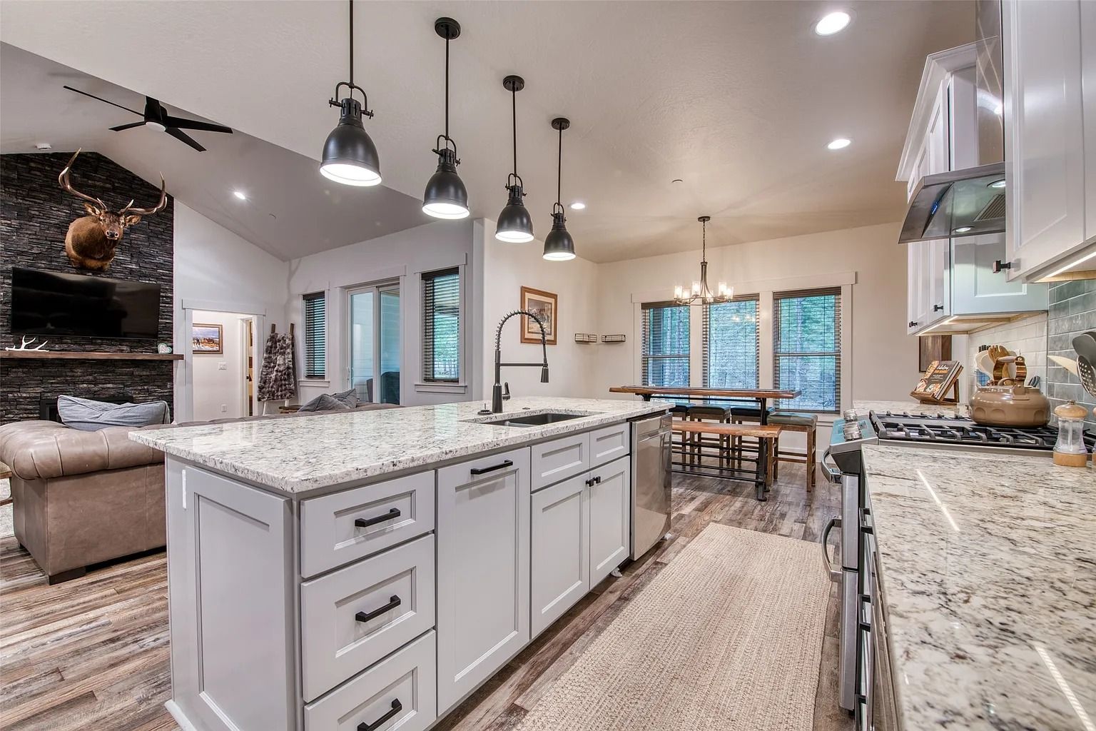 Bright modern kitchen with white cabinets, granite island, pendant lights, and dining area in the background