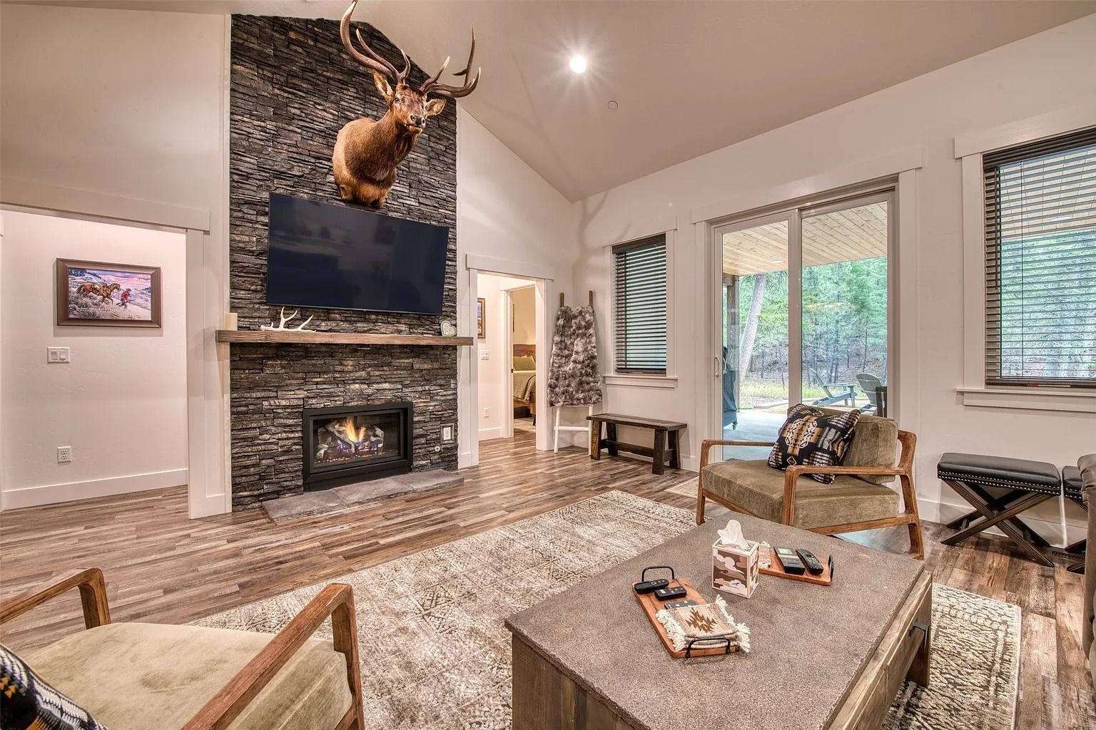 Stylish living room with stone fireplace, mounted TV, tan sofas, and large windows with blinds