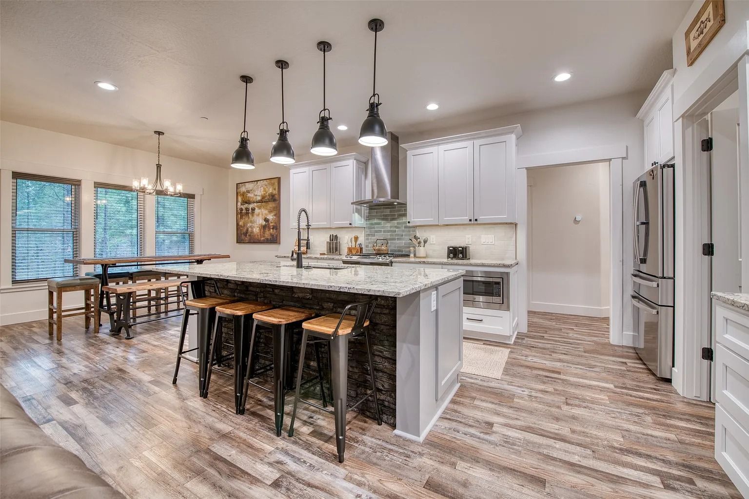 Bright modern kitchen with marble island, black pendant lights, bar stools, and wood flooring