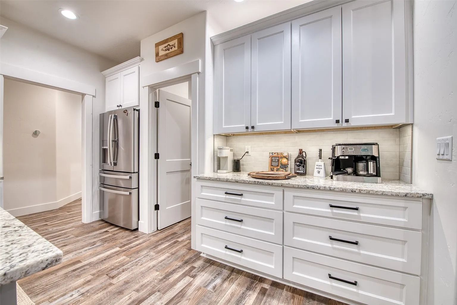 Bright modern kitchen with white cabinets, stainless fridge, and light wood flooring