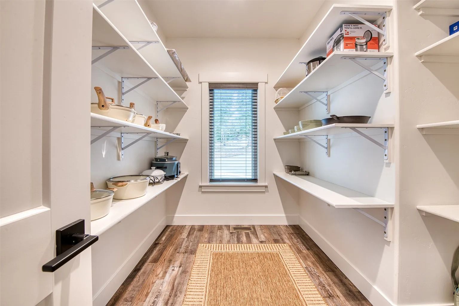 Narrow pantry with white shelves, woven baskets, and a patterned rug.