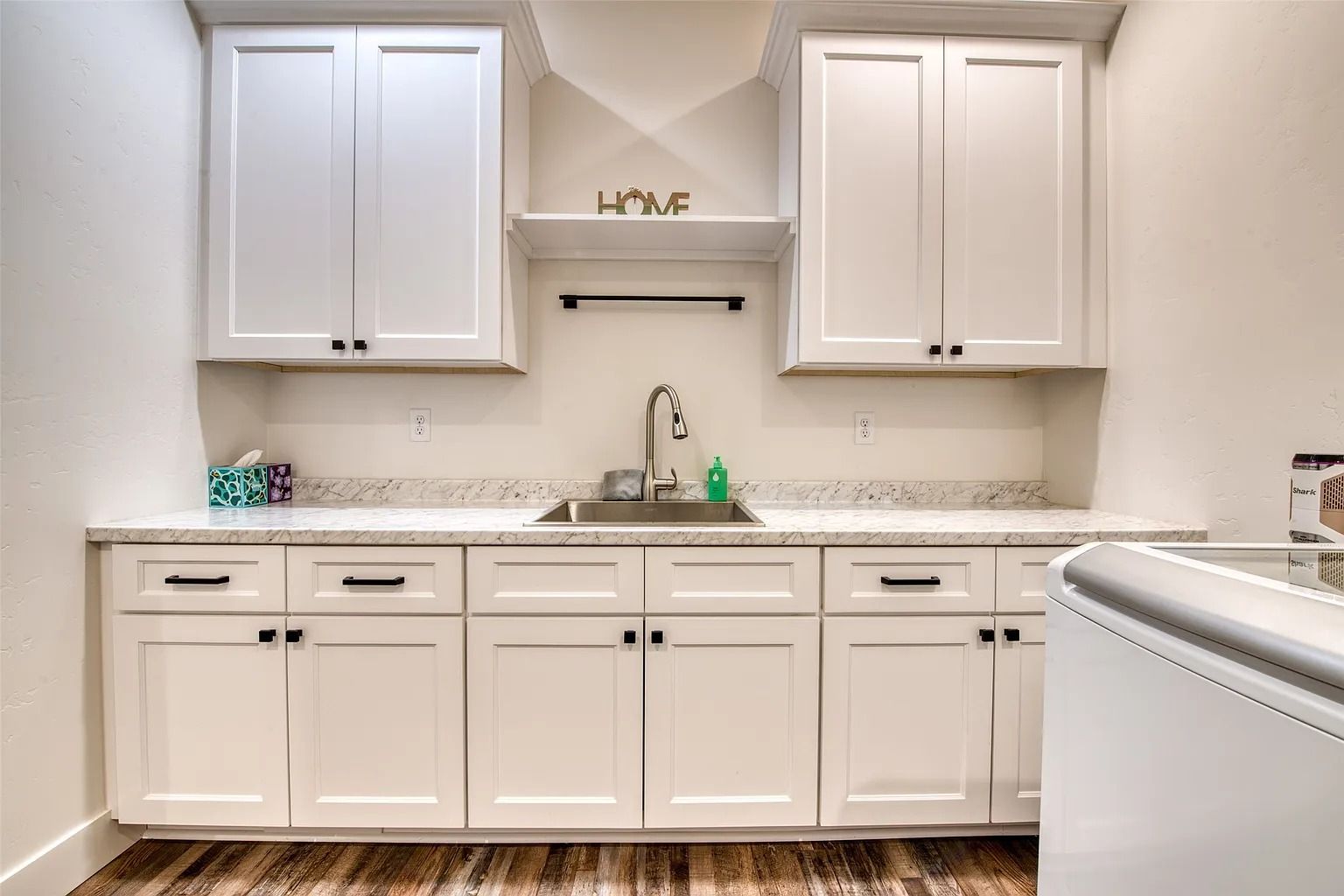 White laundry room with cabinets, sink, countertop, and washer on the right.