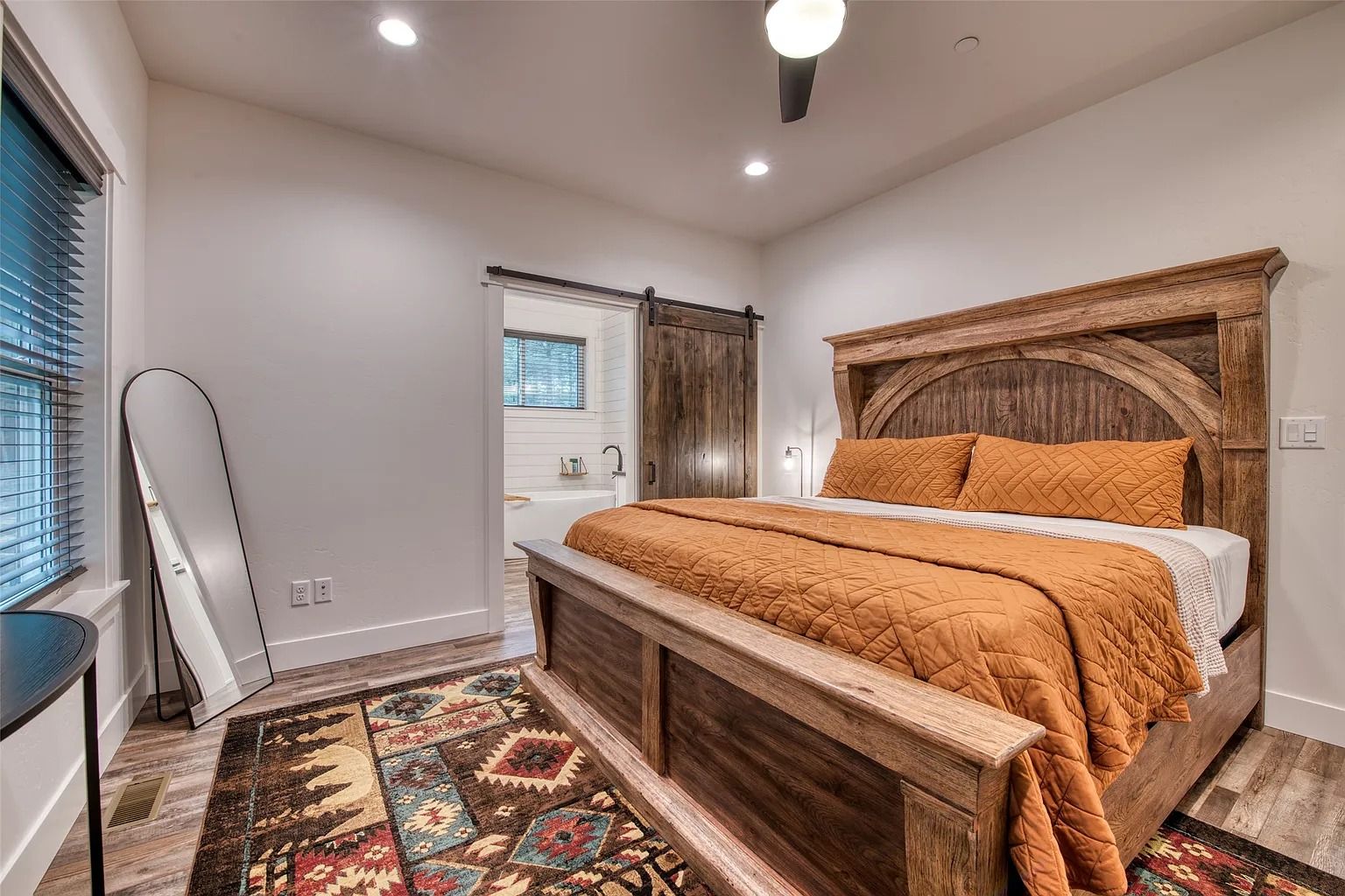 Cozy bedroom with rustic wood bed, patterned rug, window, and mirrored closet door