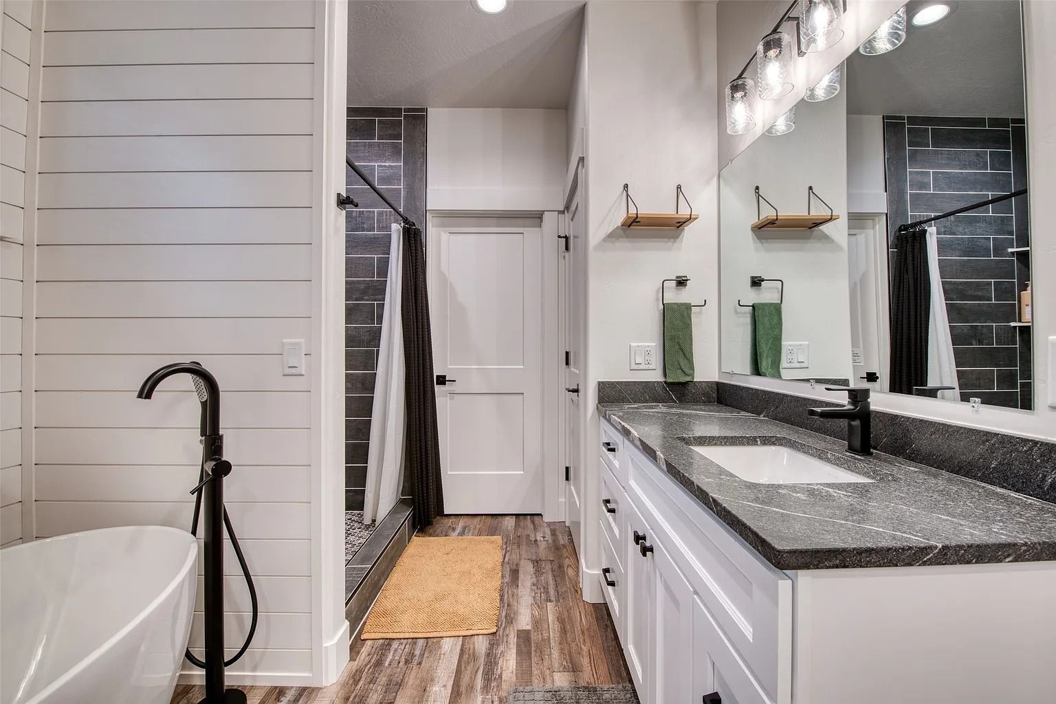 Modern bathroom with double vanity, large mirror, freestanding tub, and glass shower