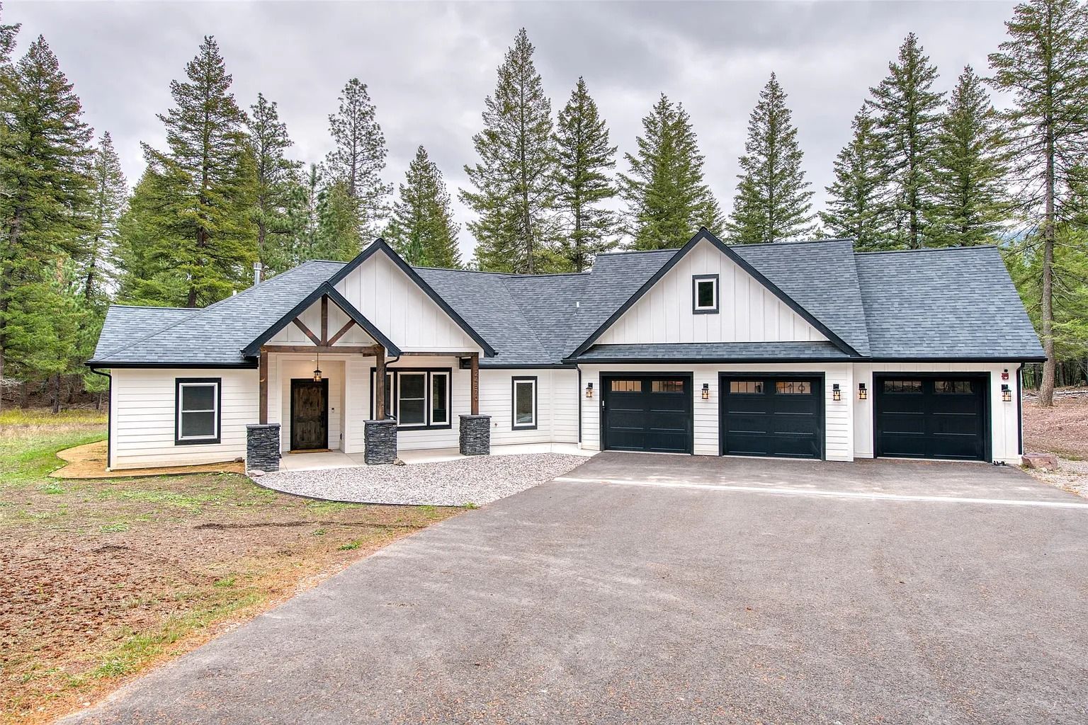 Modern single-story house with gray roof, three-car garage, and wooded surroundings