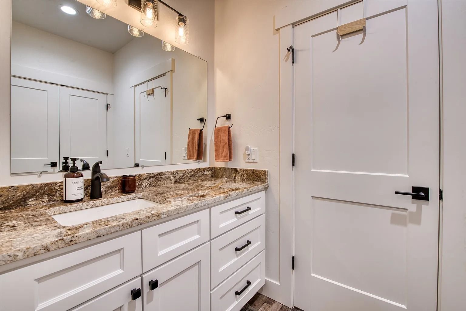 Bright bathroom vanity with granite countertop, large mirror, and white door beside it
