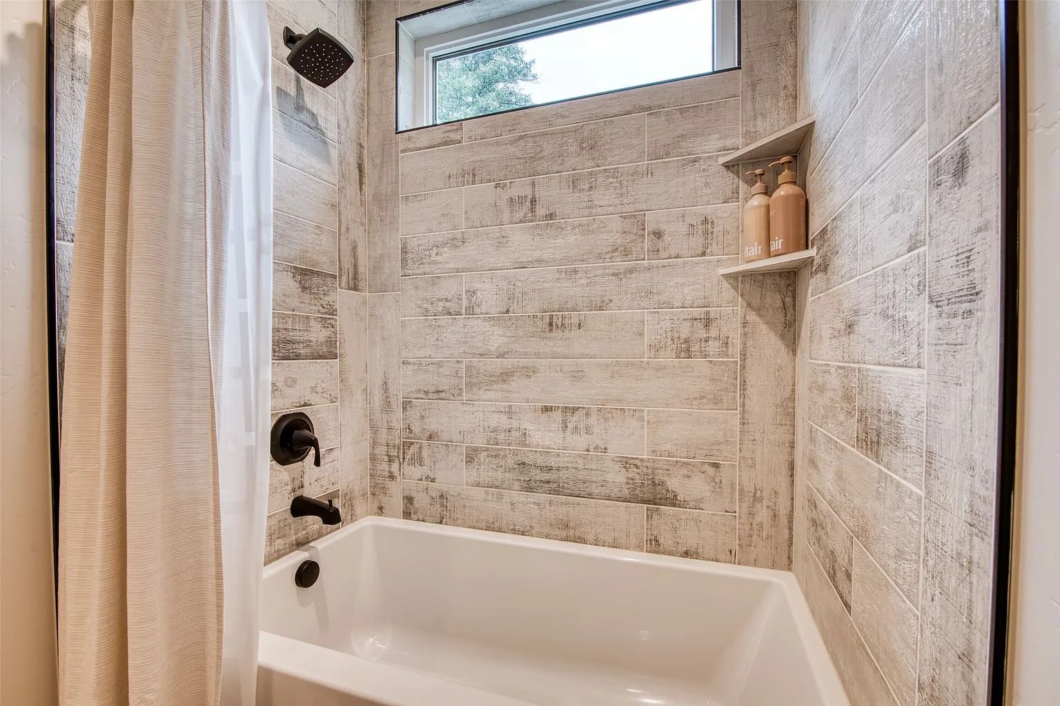 Small bathroom with a white tub, tiled shower walls, and a narrow window above.