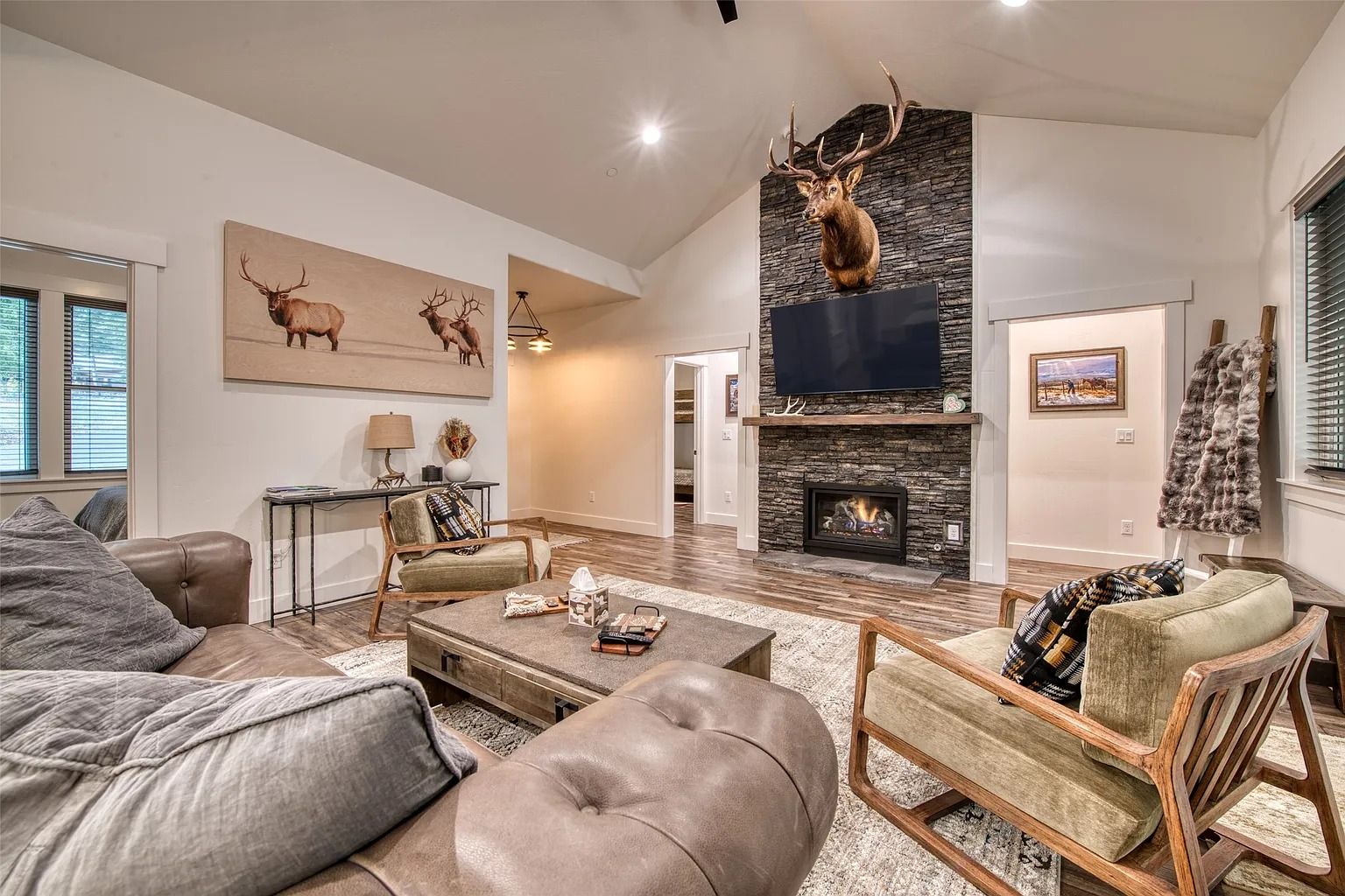 Cozy living room with gray sofas, stone fireplace, antler decor, and warm neutral tones