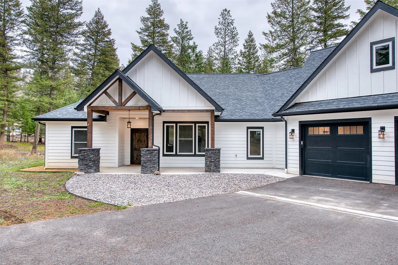 Modern white house with gray roof, stone entry, garage, and forested yard