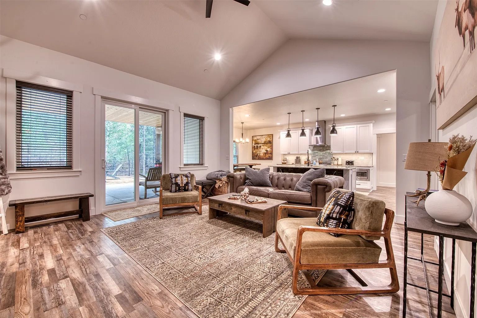 Bright living room with vaulted ceiling, fireplace, woven chairs, and open kitchen in the background