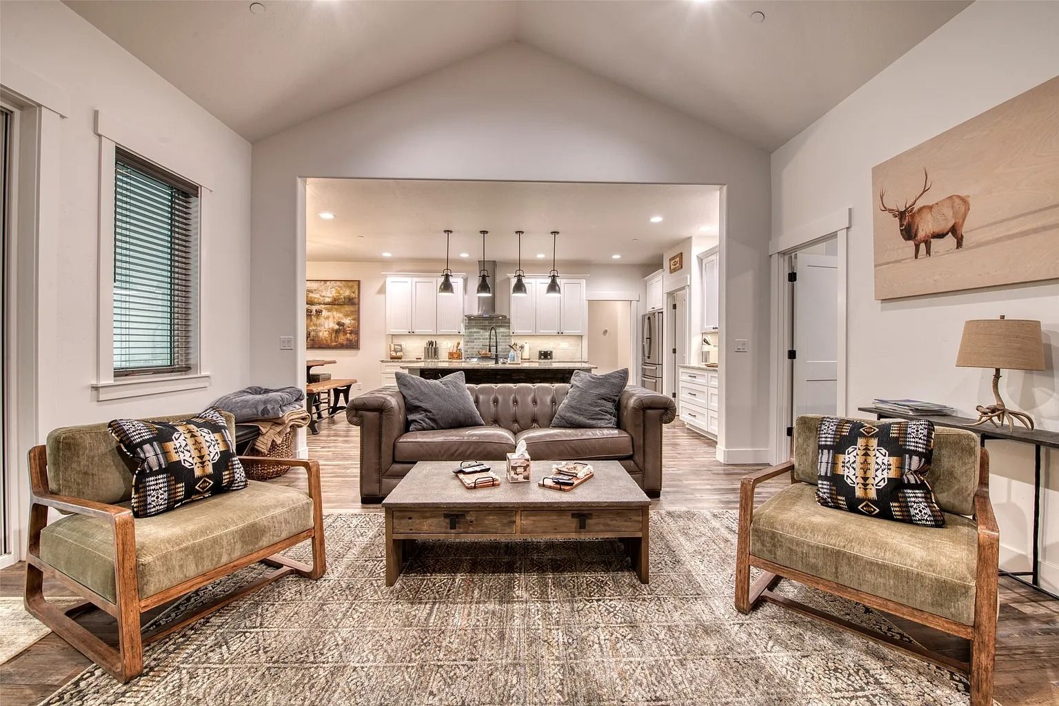 Bright living room with two wicker chairs, gray sofa, coffee table, and open view to a modern kitchen.