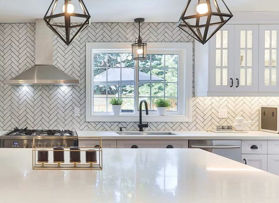 Bright modern kitchen with white cabinets, herringbone backsplash, island, and pendant lights