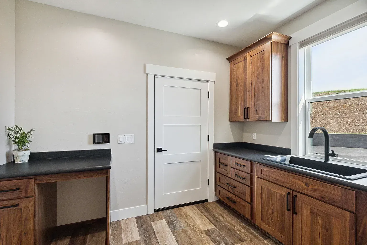 Modern kitchen with dark wood cabinets, black countertops, white door, and large window.