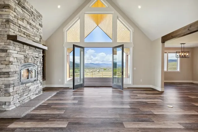 Modern living room with stone fireplace, dark wood floors, and open French doors to a scenic view
