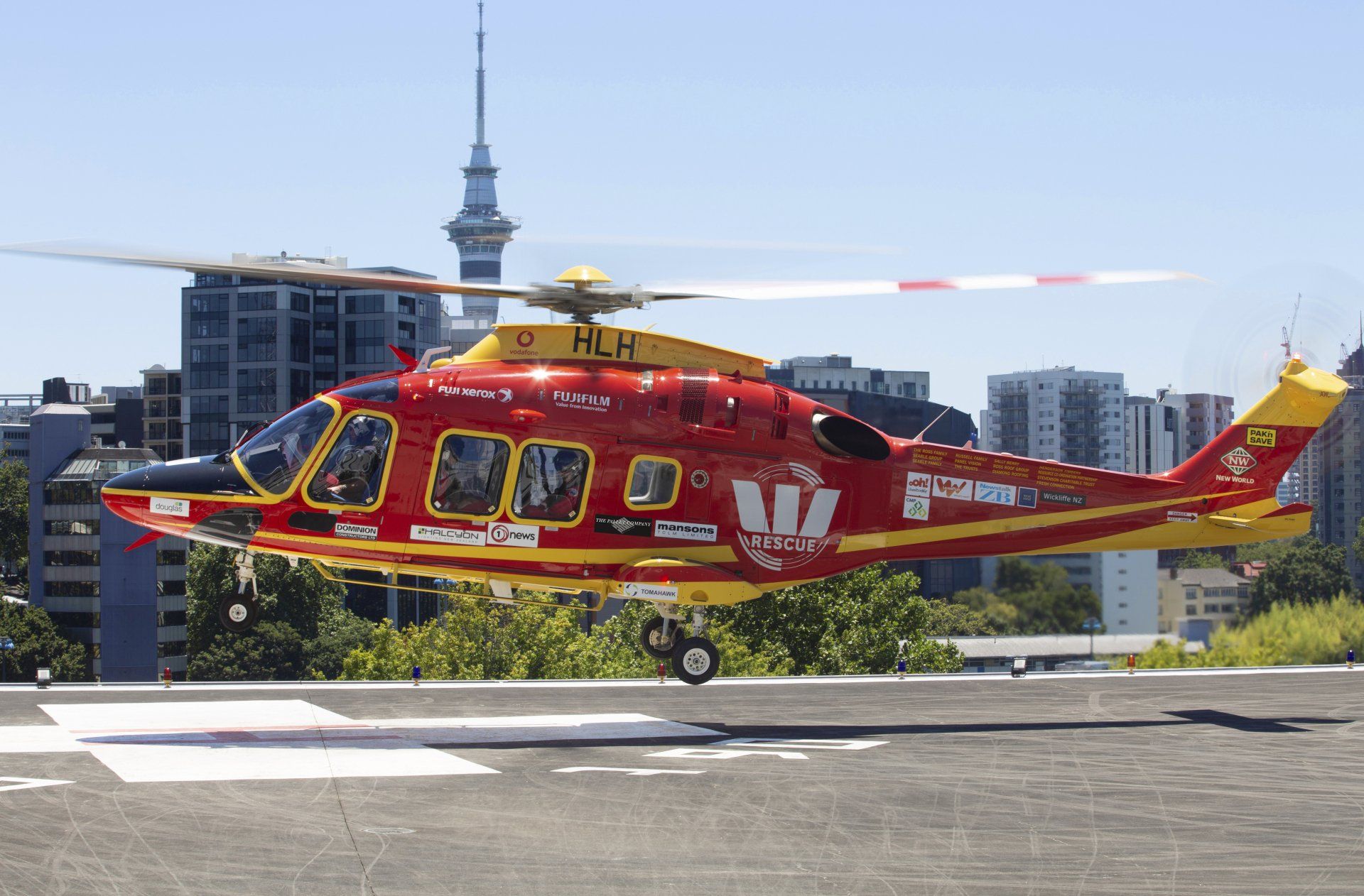 Red rescue helicopter on a rooftop helipad with city buildings and a tower in the background