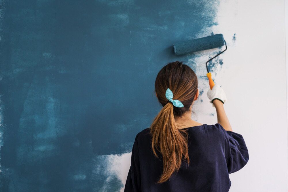A Woman is Painting a Wall With a Paint Roller — Prota NT in Howard Springs, NT