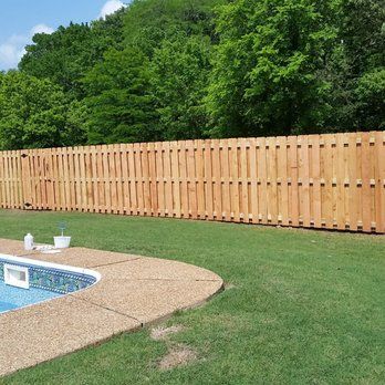 A wooden fence surrounds a swimming pool in a backyard.