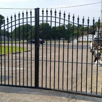 A black wrought iron gate is open to a parking lot