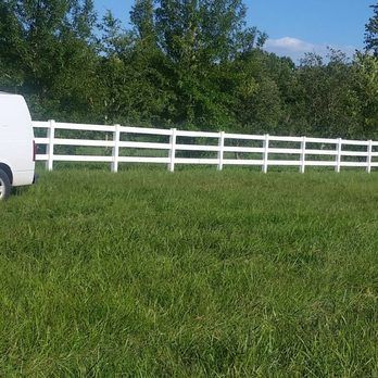 A white van is parked in a grassy field next to a white fence.