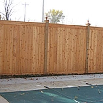 A wooden fence surrounds a swimming pool with a green cover.