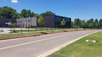 A large building is behind a fence on the side of a road.