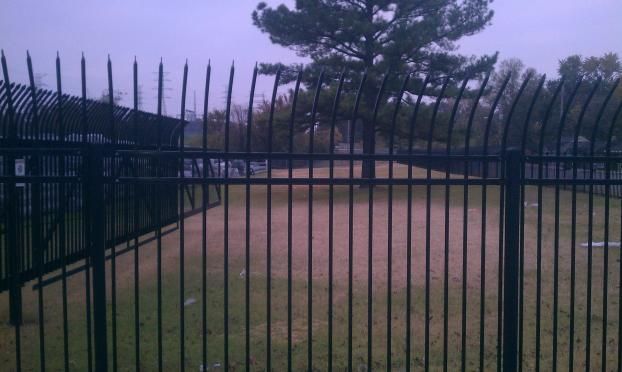 A black wrought iron fence surrounds a baseball field.